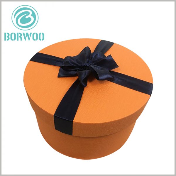 large cardboard round tube boxes with lids.Orange packaging background, black silk scarf as a gift knot